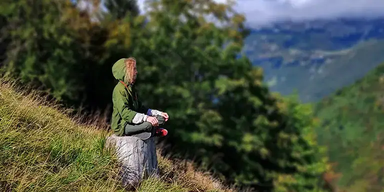 Jean Frumen meditates on a tree stump in a sunny mountain landscape.